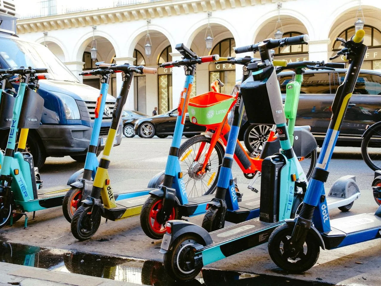 Un scooter électrique stationné en ville, casque sur le siège et immeubles en arrière-plan.