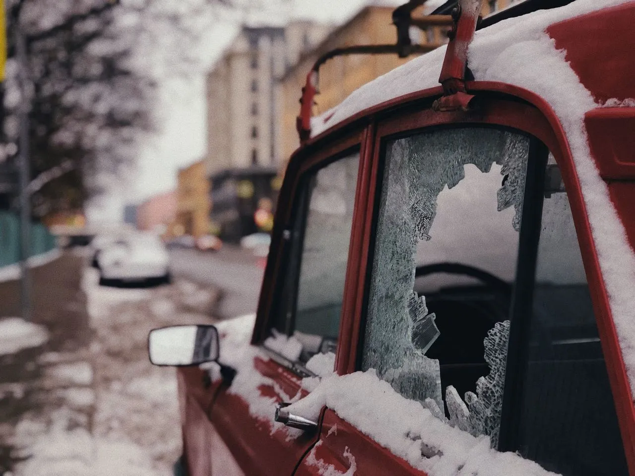 Une voiture garée devant un immeuble, portière forcée et traces d'effraction visibles.